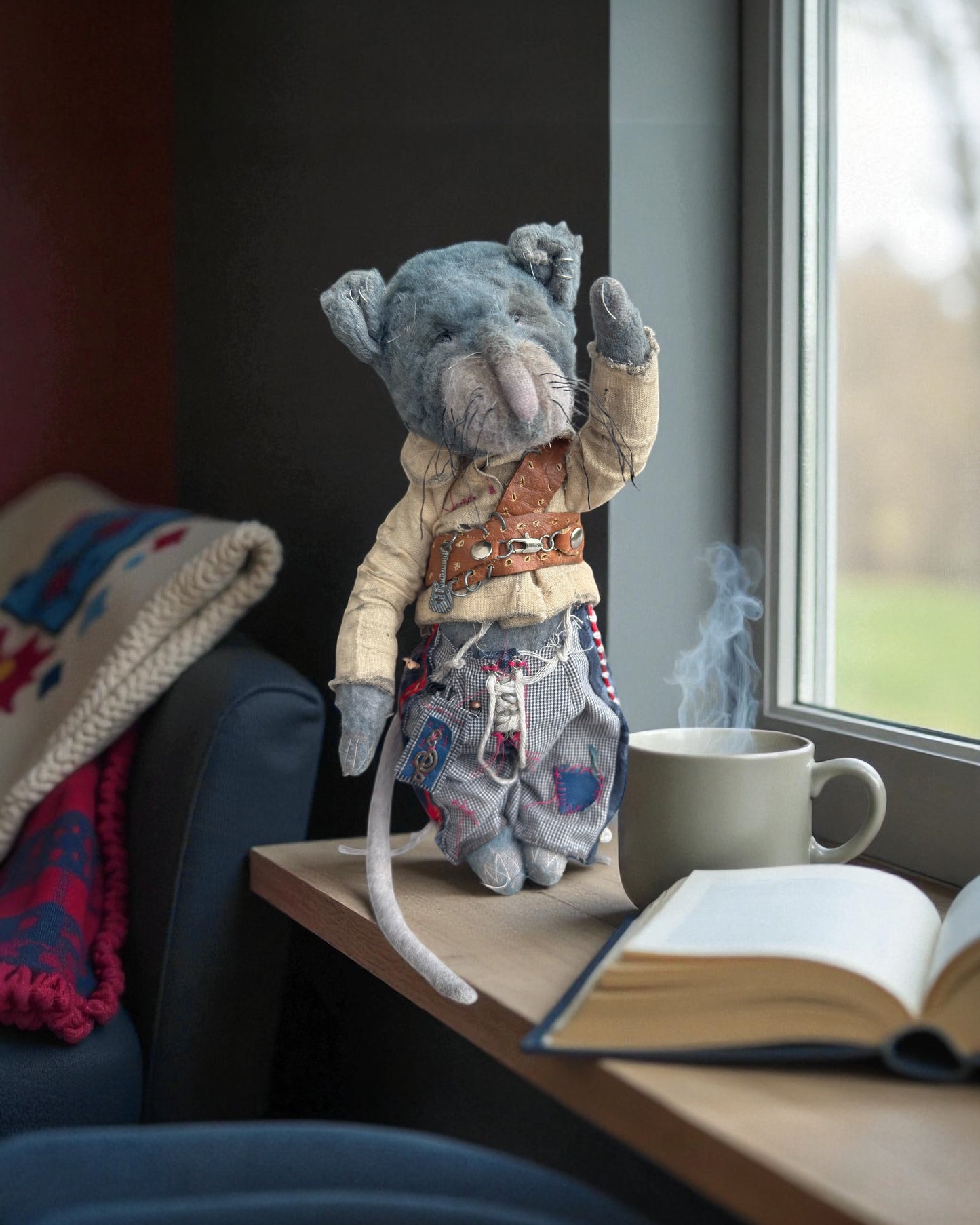 Milo the blue handmade plush mouse sitting near a window with a warm drink.